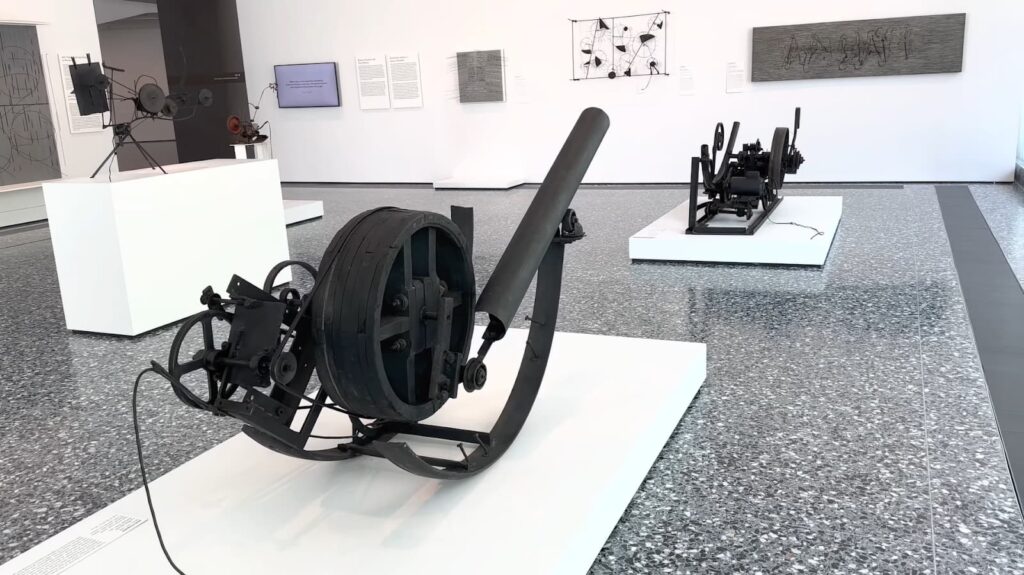 An exhibit of a black, industrial-looking machine in a contemporary art museum